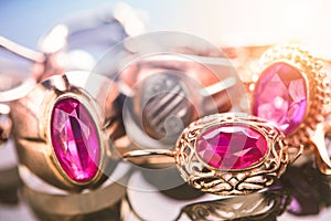 Elegant luxury composition of gold jewelry with ring with red amethyst and ruby gemstone and diamonds on light background close-up