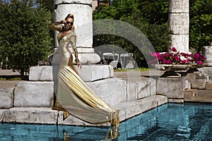 Elegant luxury evening fashion. Glamour, stylish elegant woman in golden long gown dress is posing in luxury hotel outdoor. Female