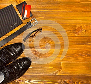 The elegant male set: men`s shoes, leather belt, on the wooden background.