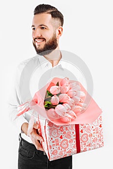 Elegant man with a beard holding a bouquet of tulips and a gift box, a gift for Valentine`s Day