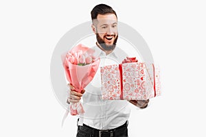 Elegant man with a beard holding a bouquet of tulips and a gift box, a gift for Valentine`s Day