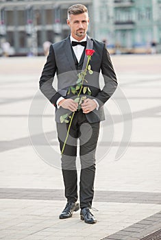elegant man in black tux. man wearing tux bowtie outdoor. full length of tux man with red rose