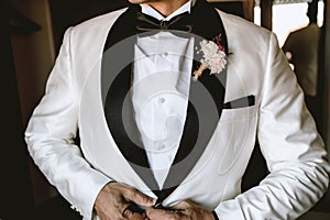 an elegant man dressing up in a white suit for his wedding, with a flower in his pocket