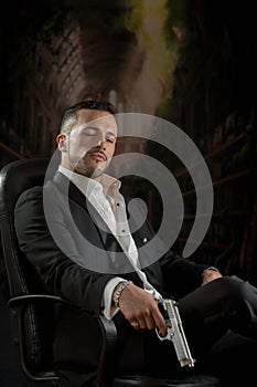 Elegant man sitting in a chair holding gun over