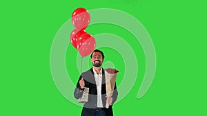Elegant man, in a suit, with a bouquet of flowers, a gift and balloons walking on a Green Screen, Chroma Key.