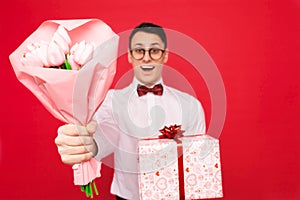 Elegant man, wearing glasses, with a gift and a bouquet of flowers, on a red background, the concept of women`s day