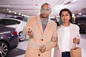 Elegant married couple in an underground parking lot opens car using alarm key fob