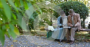 Elegant, married elderly couple relaxing on park bench and looking at photoalbum