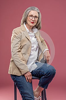 Elegant mature woman in beige jacket sitting on a chair