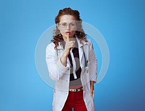 Elegant medical practitioner woman showing shh gesture on blue