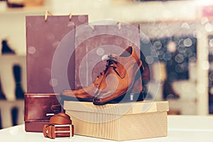 Elegant men leather shoes, belt, wallet, and shopping bags in a background on the shelf at the shoe store