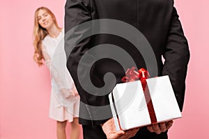 Man in a suit makes a surprise to a woman, gives a bouquet of flowers and a box with a gift, on a pink background of women`s day