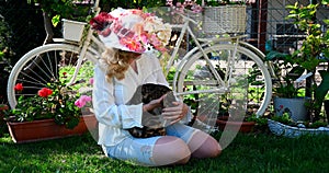 Elegant middle age woman sitting in the grass reading book in the romantic provence decoration garden playing with bengal cat
