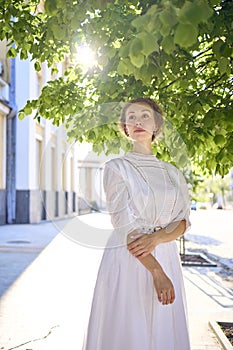 elegant middle age woman in a white vintage dress against the background of historical buildings in the morning light