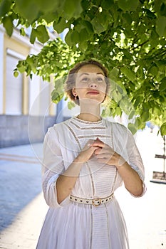 elegant middle age woman in a white vintage dress against the background of historical buildings in the morning light