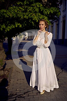 elegant middle age woman in a white vintage dress against the background of historical buildings in the morning light