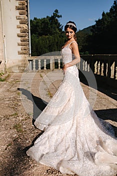 Elegant model in wedding dress posing to photographer outdoors. Beautiful young woman with fashion makeup