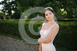 Elegant model in wedding dress posing to photographer outdoors. Beautiful young woman with fashion makeup