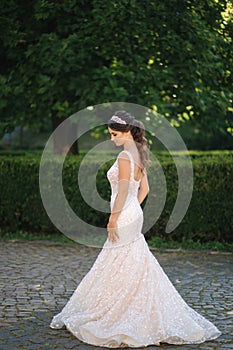 Elegant model in wedding dress posing to photographer outdoors. Beautiful young woman with fashion makeup