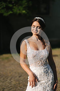 Elegant model in wedding dress posing to photographer outdoors. Beautiful young woman with fashion makeup