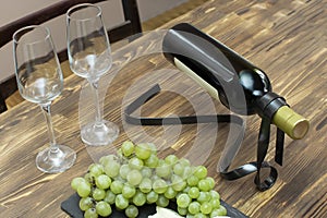 Elegant modern metal red white wine bottle holder on wooden table with glasses, brie cheese, grapes on black slate board