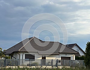 Elegant modern private single-family house with brown roof and metal fence.