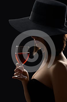 Elegant mysterious woman in a hat holding a glass of red wine on