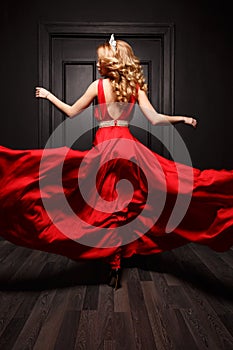 Elegant and passionate woman with tiara on her head in the red evening fluttering dress is capture in move, spinning