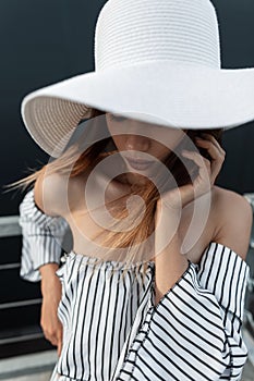 Elegant portrait sexy young model woman in beautiful white fashionable hat outdoors in city. Woman in summer fashion striped