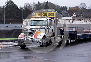 Elegant powerful big rig semi truck with step down flat bed trailer on construction side