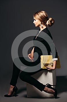 Elegant pregnant woman sitting against black studio background.