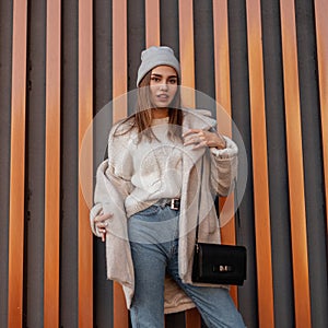 Elegant pretty modern young woman in fashionable spring clothes with a leather black stylish handbag stands near a striped metal