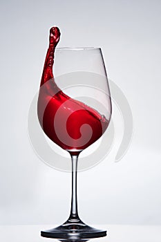 Elegant pure wineglass with wave of brightly red wine standing against light background with reflection in down.