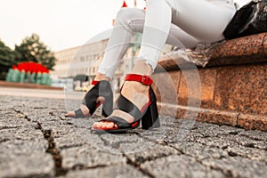 Elegant red-black sandals with heels on female legs, close-up