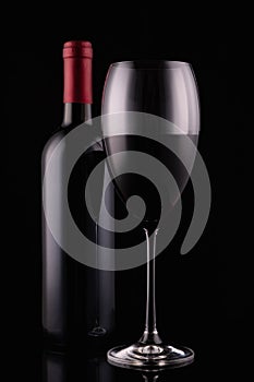 Elegant red wine glass and black wine bottle on black  background