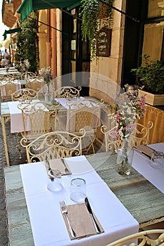 elegant restaurant, metal restaurant chairs, tables set in front of a restaurant, flowers in vases on tables, cutlery and napkins