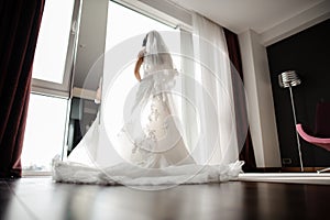 Bride in wedding dress and silk veil looking through the window