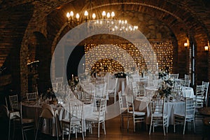 Elegant, romantic table setting for indoor wedding reception with fairy lights on wall behind. Winery, brewery cellar