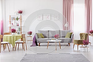 Elegant daily room with round table with wooden chairs and grey sofa with olive green pillows, stylish armchair next to it