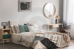 Elegant round mirror in wooden frame above fancy console table with flowers in vase in trendy bedroom interior with beige vase photo