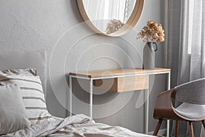 Round mirror in wooden frame above fancy console table with flowers in vase in trendy bedroom interior with beige vase