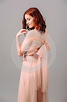 Elegant salmon dress. Beautiful peach chiffon evening gown. Studio portrait of young brunette woman.