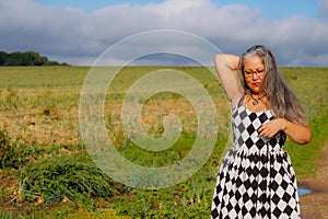 Elegant senior adult woman standing in field, touching her head and looking down