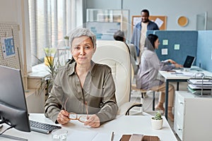 Elegant senior businesswoman working at desk in open office and smiling