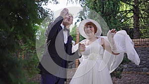 Elegant senior groom blowing soap bubbles outdoors as cheerful bride laughing in slow motion. Happy loving Caucasian