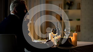 Elegant senior man sitting at served table, waiting for woman, anniversary date