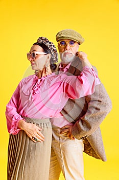 Elegant senior married couple. Beautiful woman and handsome man posing with stylish matching clothes against yellow