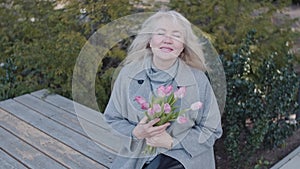 An elegant senior woman with tulips in a city yard