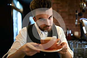 Elegant serious barista holding cup with lavender cappuccino.