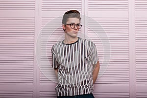 Elegant serious young man hipster in fashionable glasses with a hairstyle in a trendy striped t-shirt stand near a vintage wooden